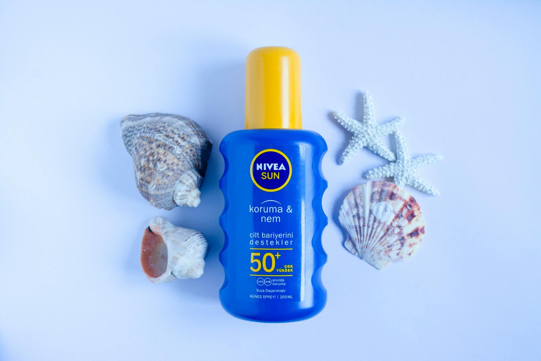 Blue Nivea Sun SPF 50+ sunscreen bottle on white background with seashells and starfish for summer skincare.