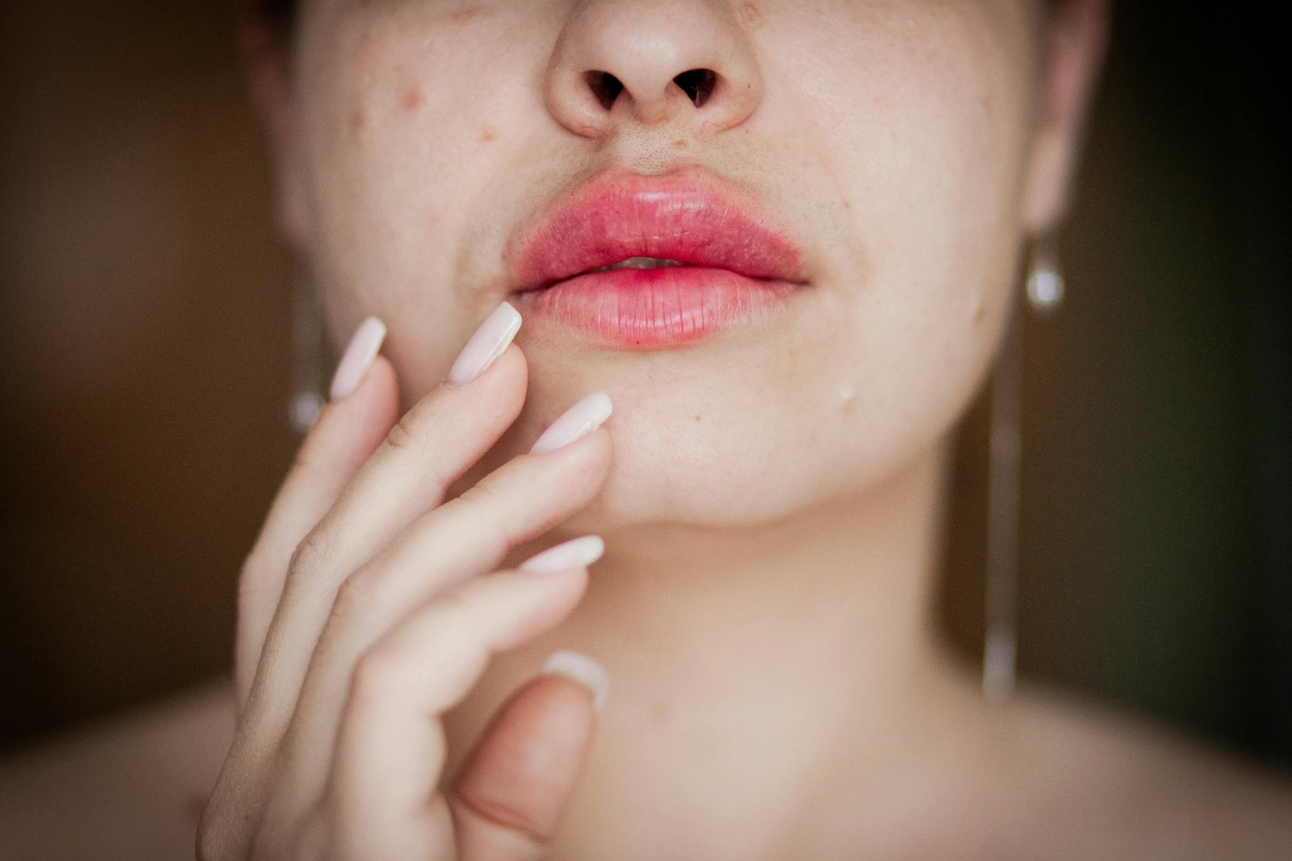 Close-up shot of a woman's lips and hand touching her face, emphasizing beauty and care.