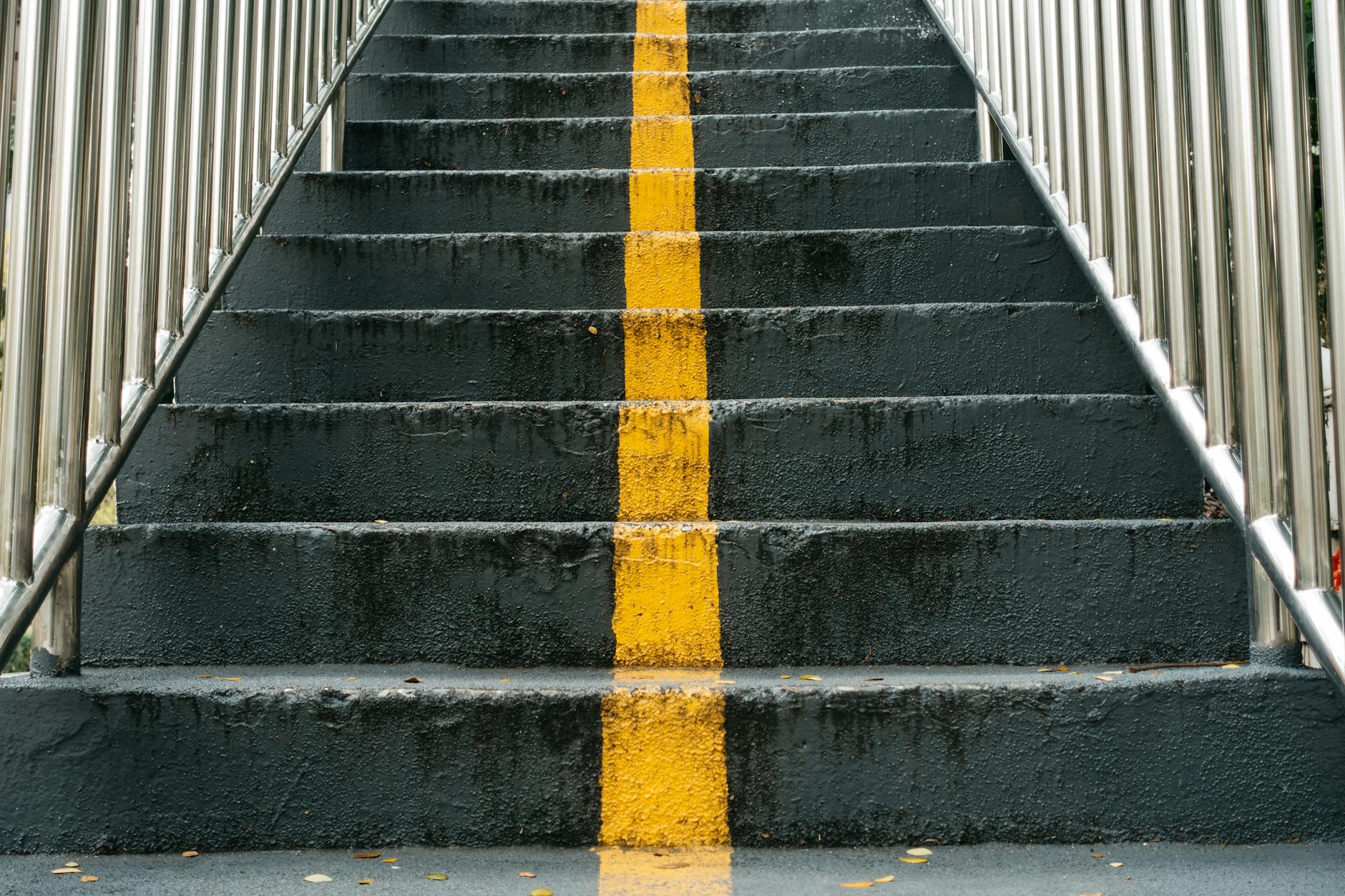 Close-up of urban staircase featuring a prominent yellow line and metal railings.