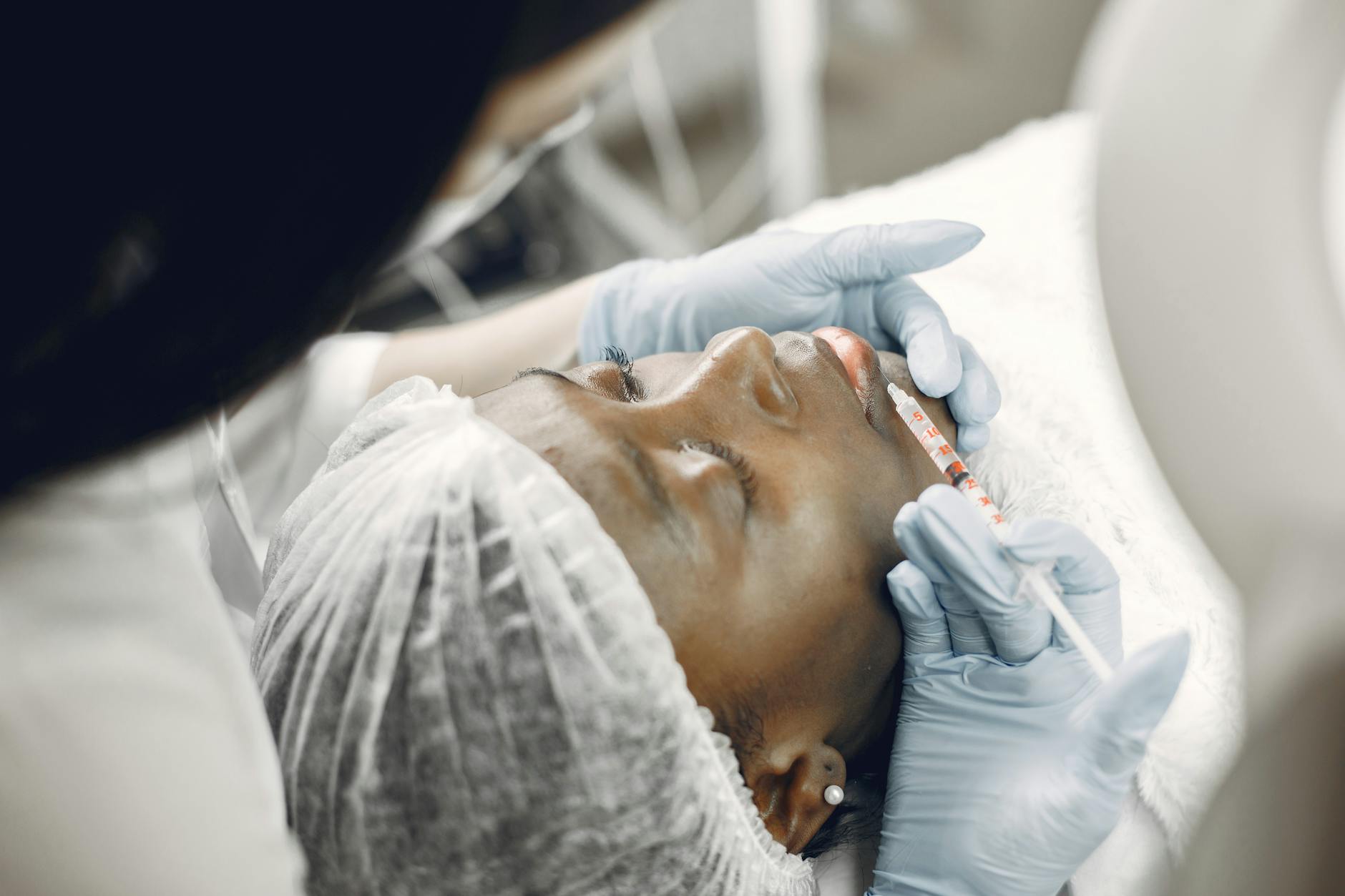 Close-up of a woman receiving a cosmetic lip injection in a clinic setting.
