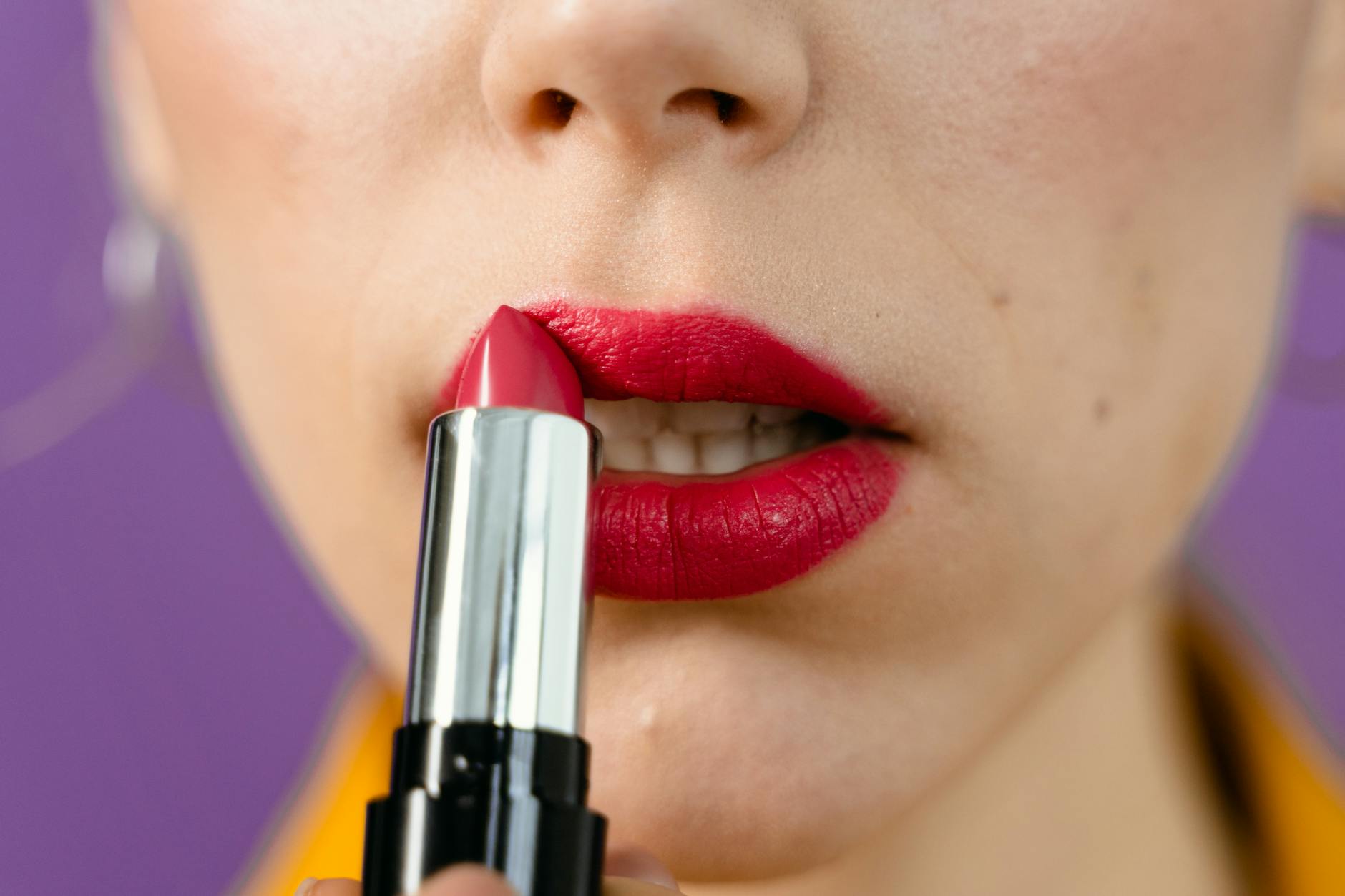 Detailed view of a woman applying vibrant red lipstick on her lips.