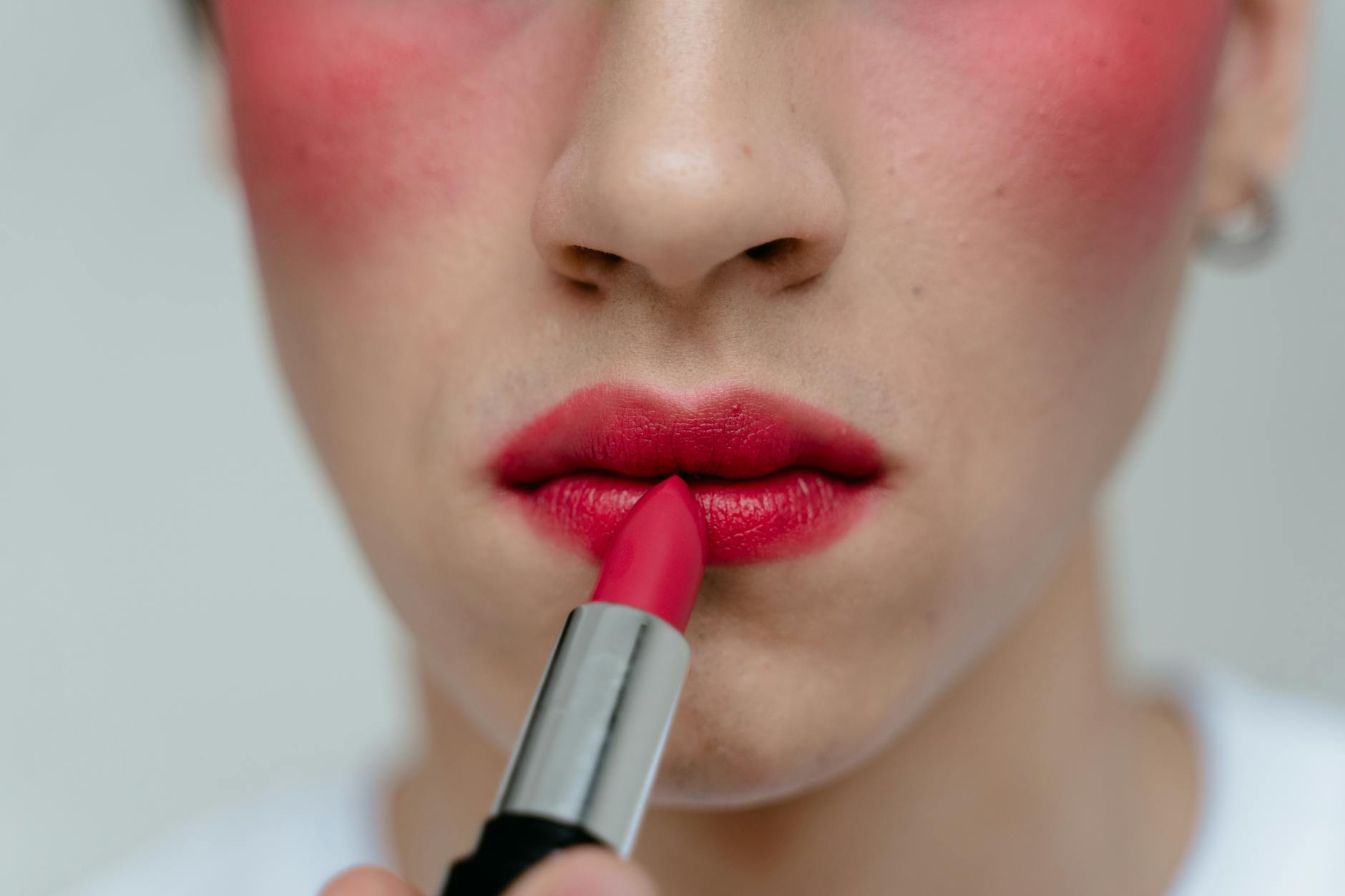Close-up view of a person applying red lipstick to their lips, highlighting vibrant makeup.