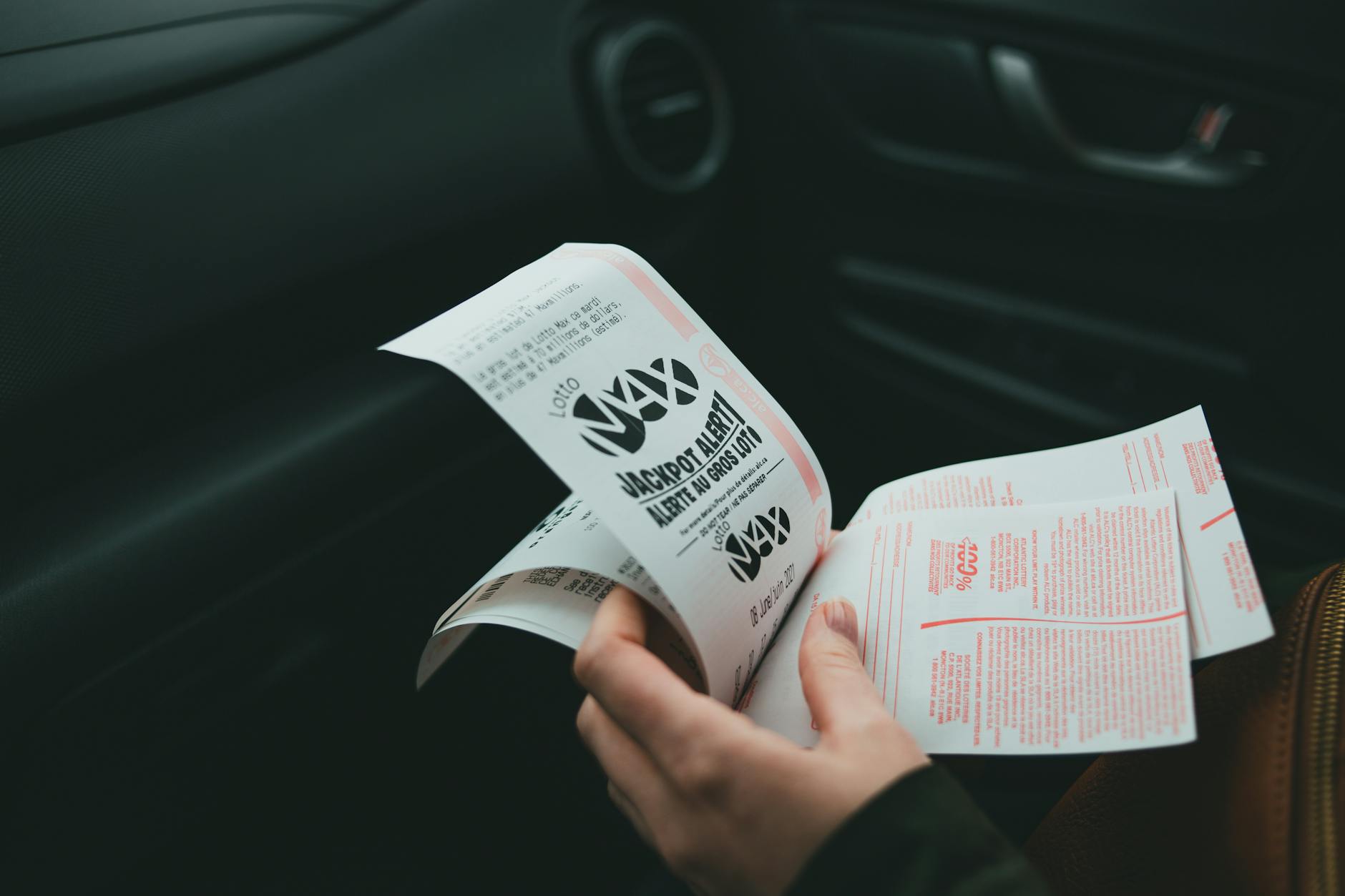 Close-up of hands holding Lotto Max papers inside a car, symbolizing luck and chance.