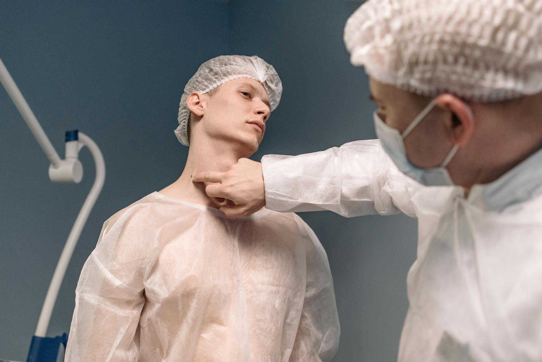 A doctor in protective gear examines a patient's neck in a sterile medical setting.