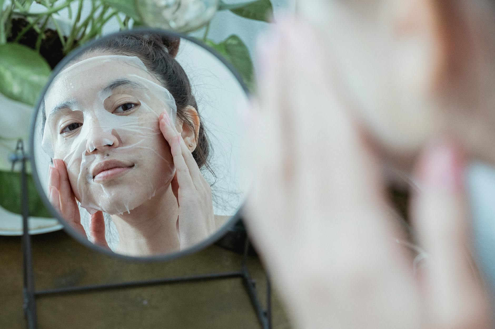 A woman in front of a mirror applying a sheet mask as part of her skincare routine.