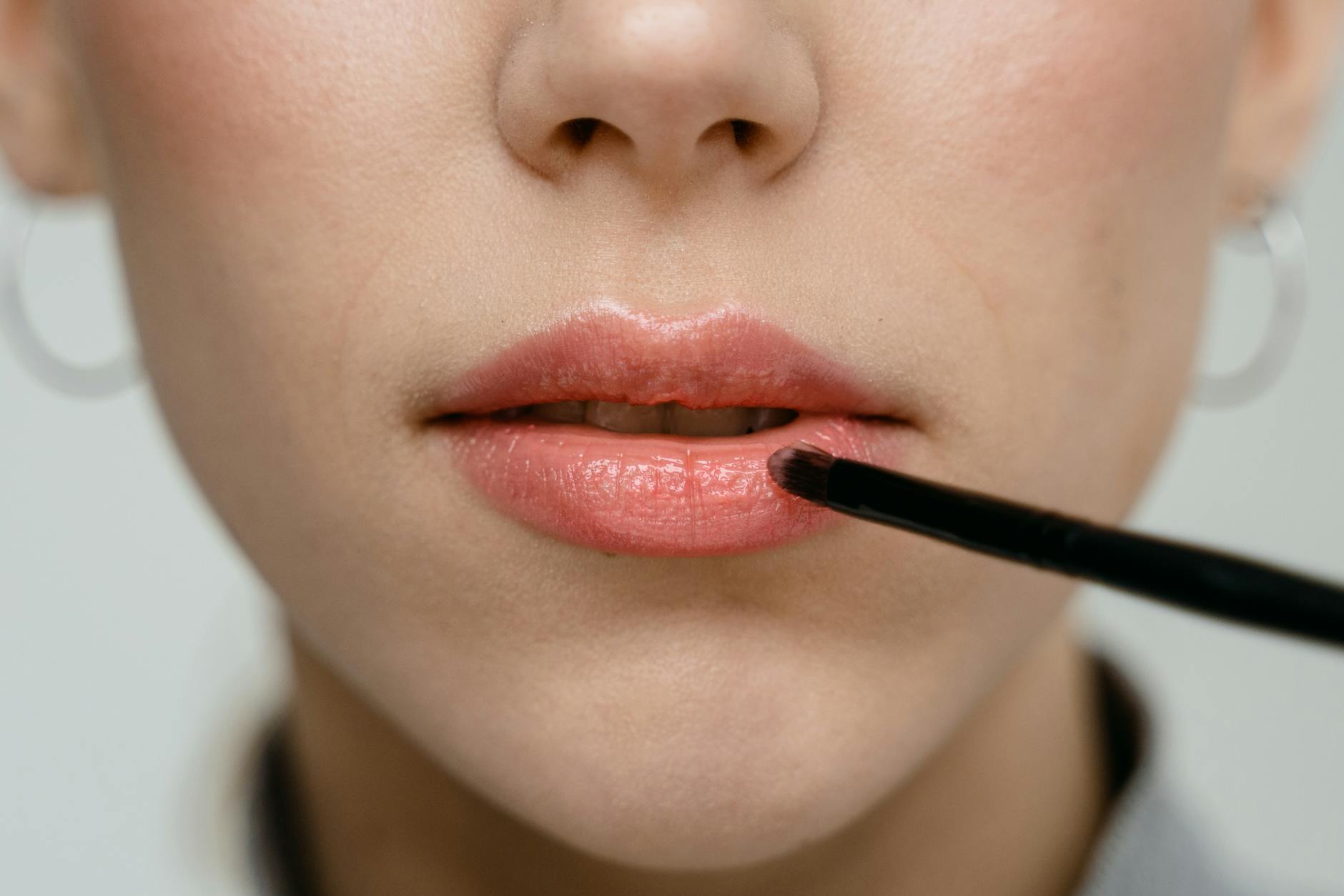 A detailed close-up of a woman applying pink lipstick with a brush.