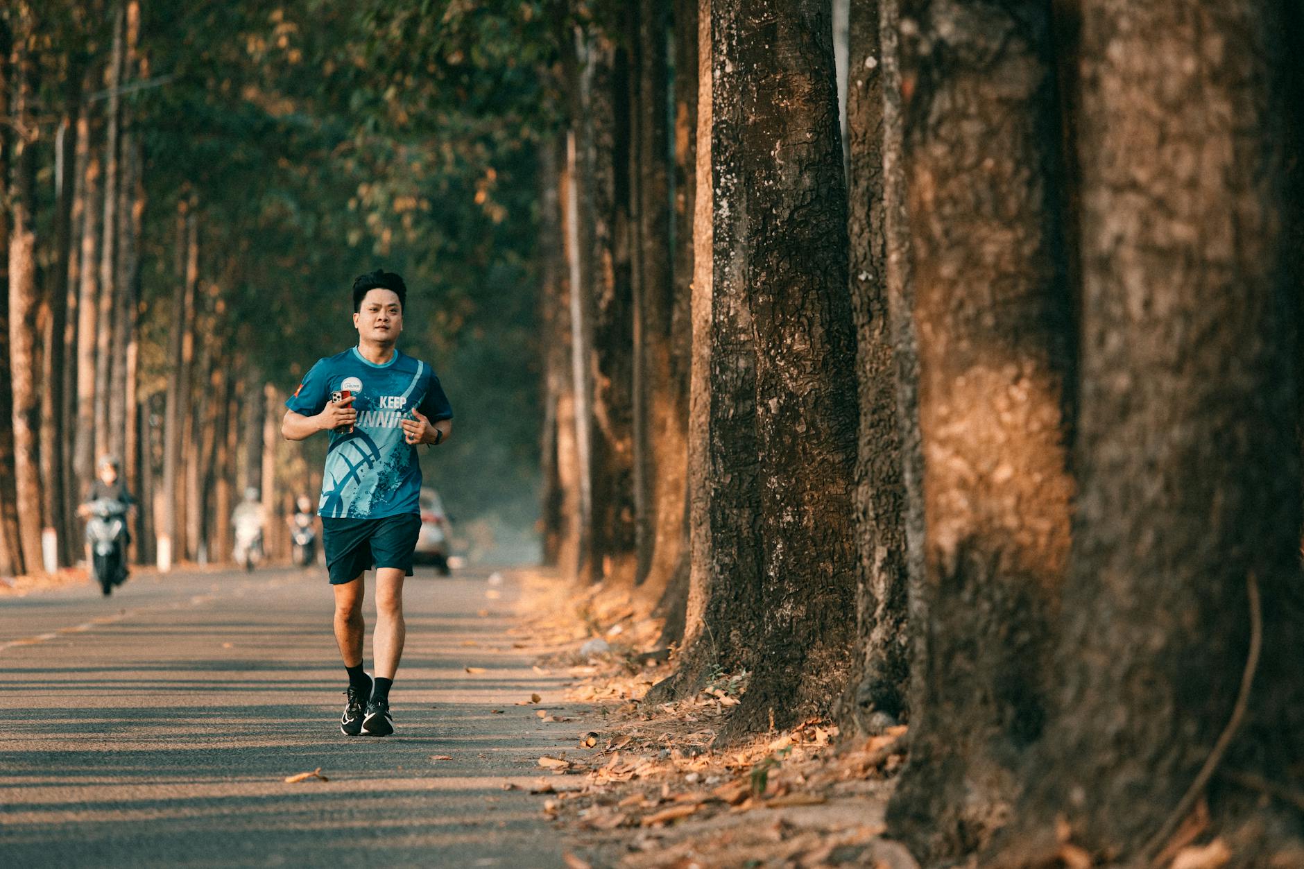 An athletic man runs along a picturesque tree-lined street during autumn. Perfect for fitness and outdoor themes.