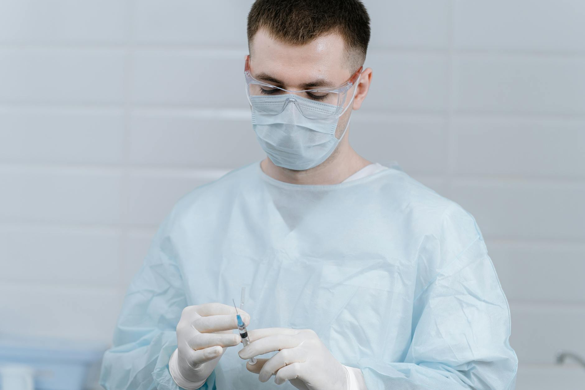 Healthcare professional wearing protective gear and preparing an injection in a medical setting.